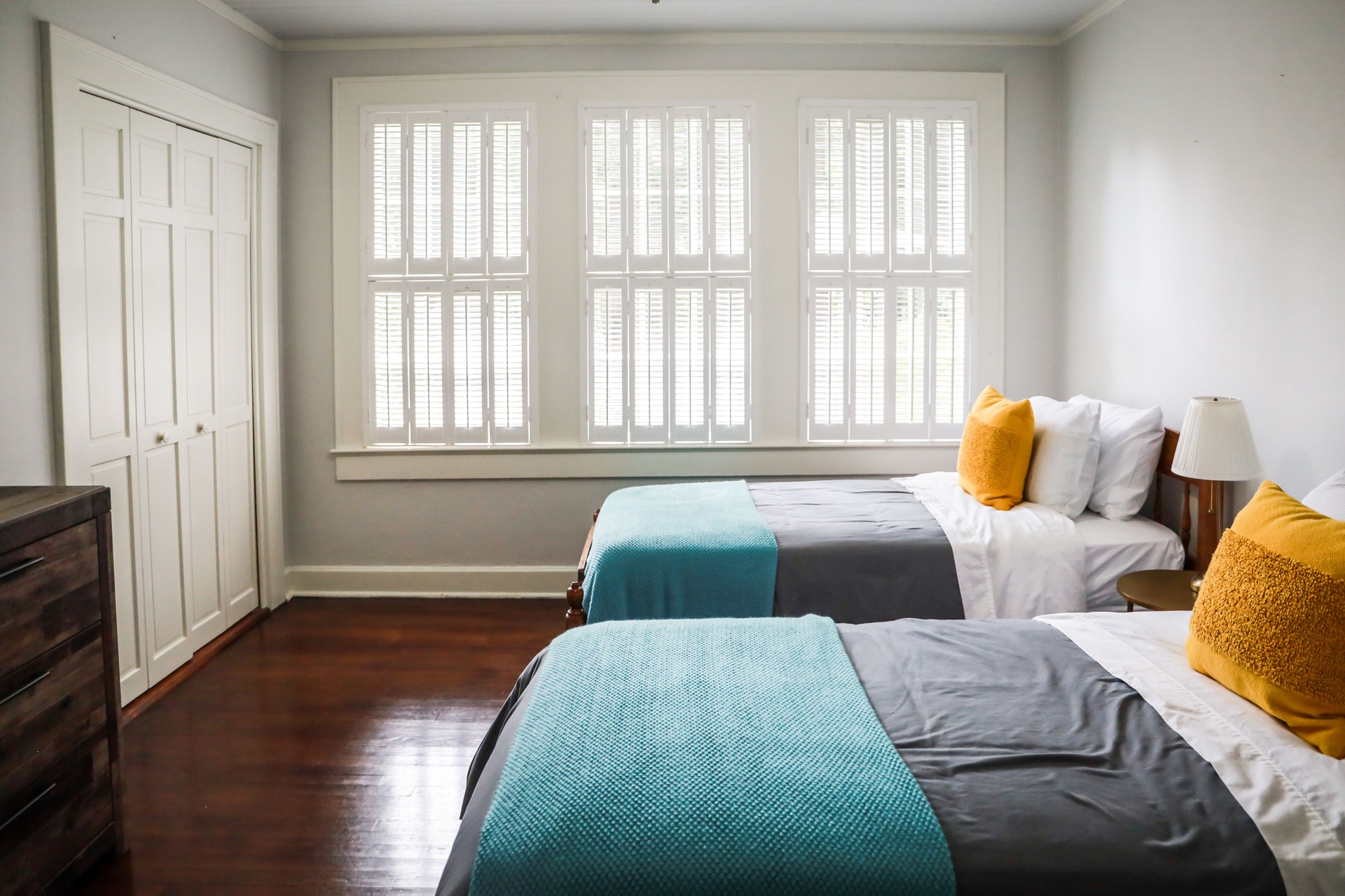 A guest bedroom with two twin beds with turquoise and gray bedspreads and yellow decorative pillows